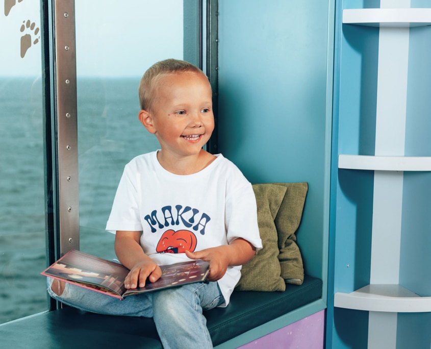 A child reading a book in the Kids room aboard Aurora Botnia